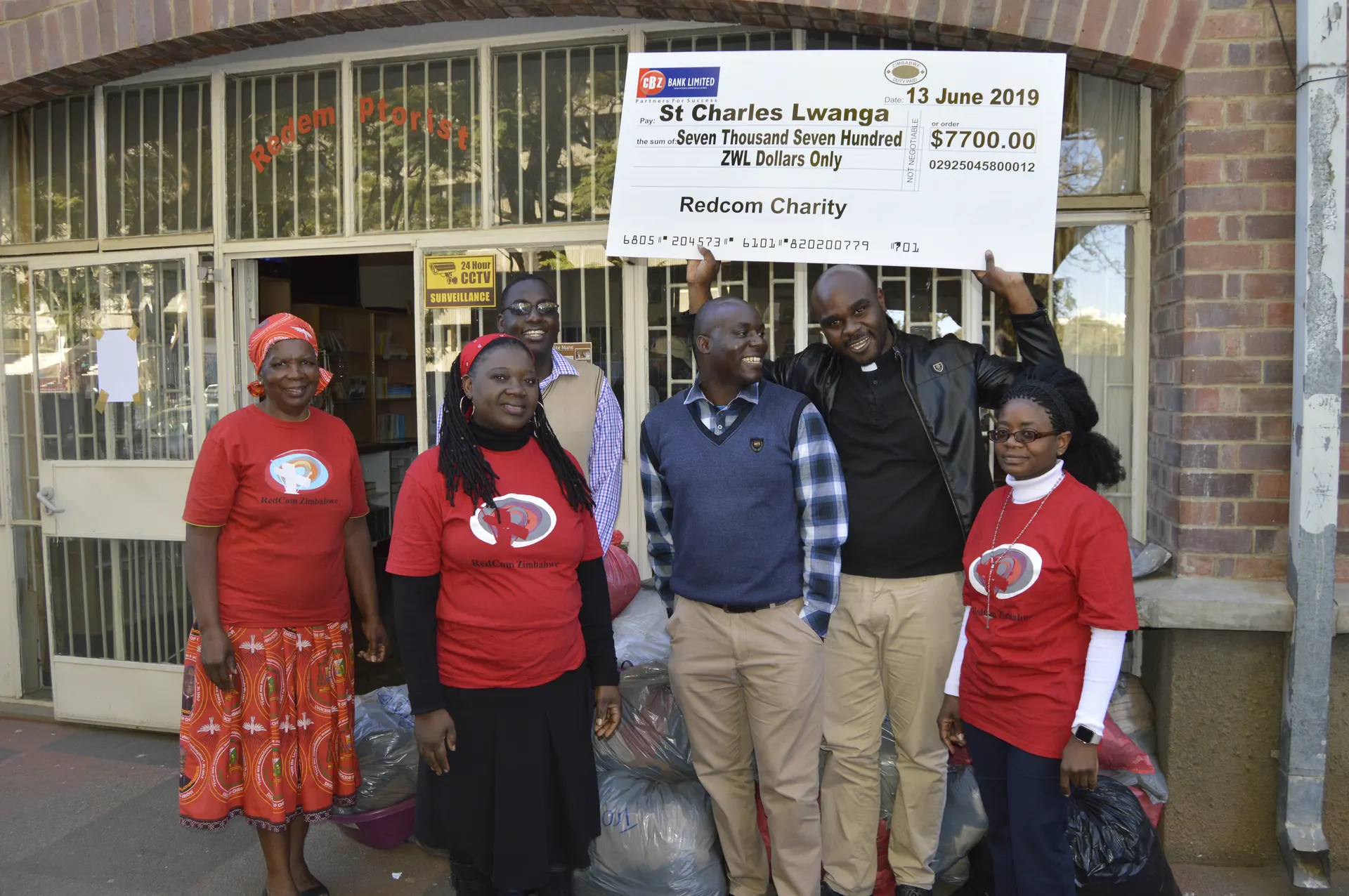 RedCom Coordinator, Mrs. Dorothy Zakeyo, Mrs. Mombo, Br. Kenneth Temba, Mr. Justice Makura, Fr. Talent Muhomba lifting the cheque and Mrs. Dhlamini pose for a picture after the presentation of goods meant for the victims of